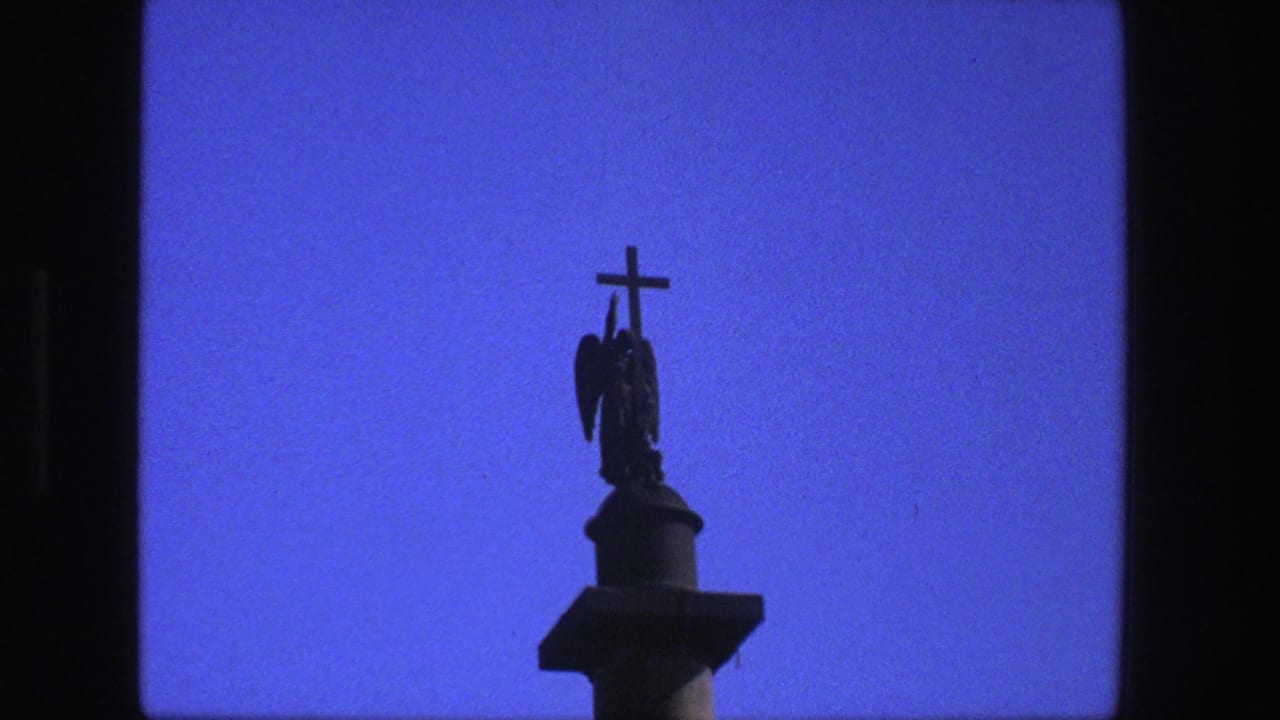 Dark crucifix and winged figure silhouetted against a blue sky.