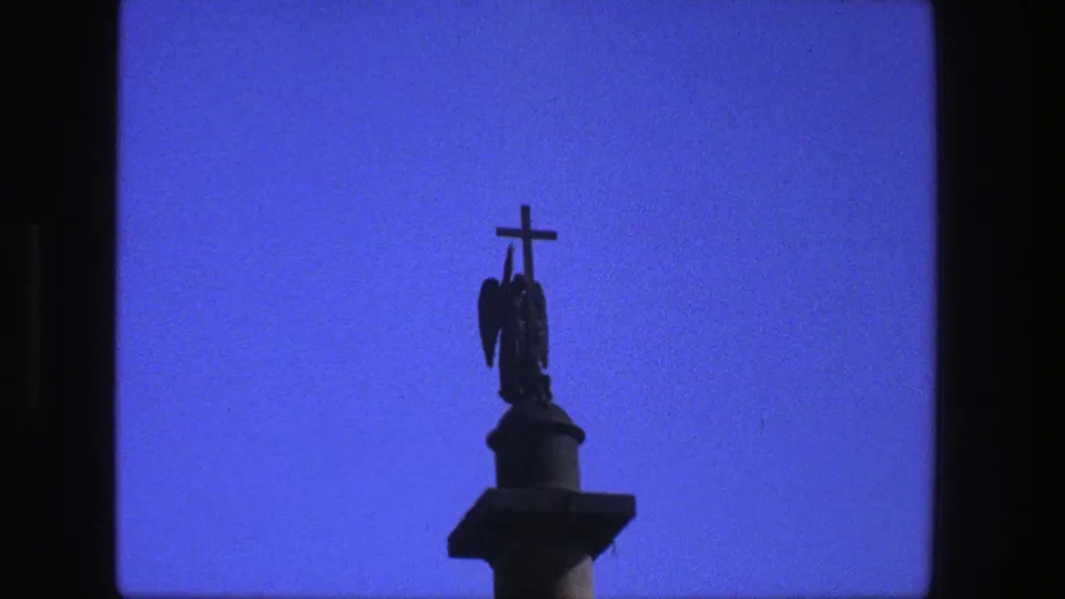 1975 Denmark 8mm frame showing a silhouetted crucifix above a winged religious figure on a pedestal against clear blue sky.
