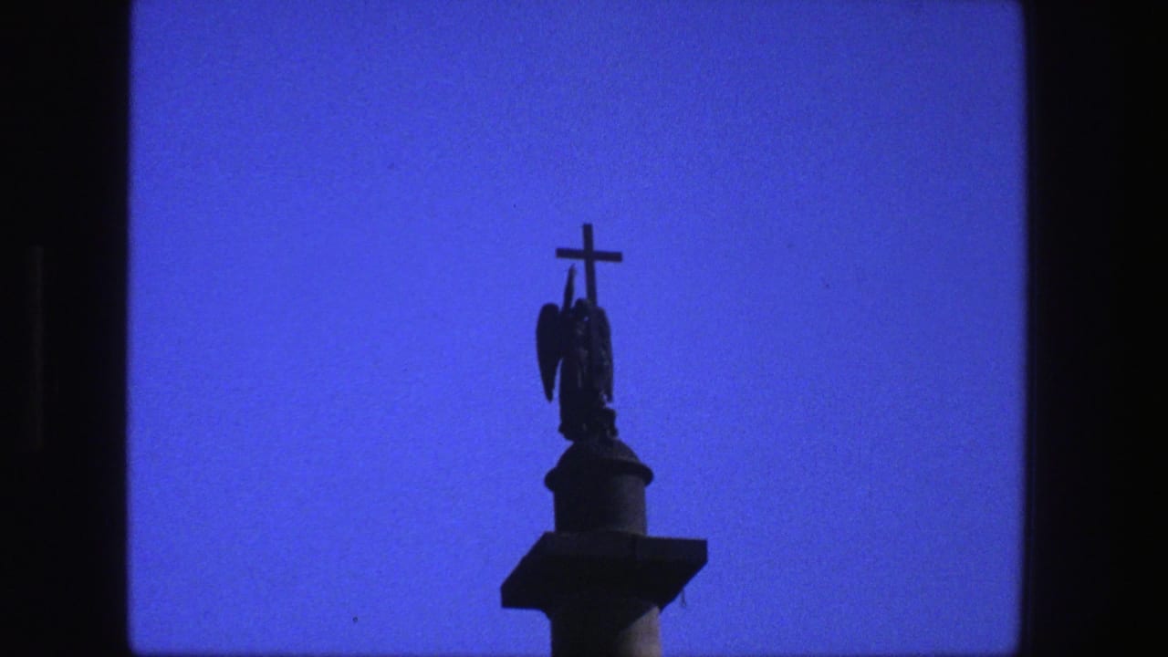 Silhouetted cross and religious statue seen against clear blue sky.