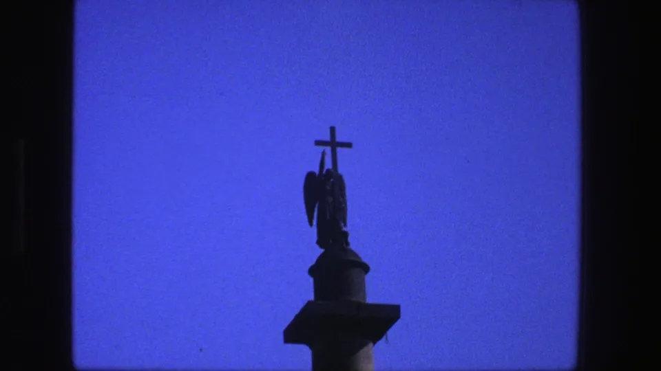 1975 Denmark 8mm frame with a dark cross and winged statue shape rising from a column against a vivid blue sky.