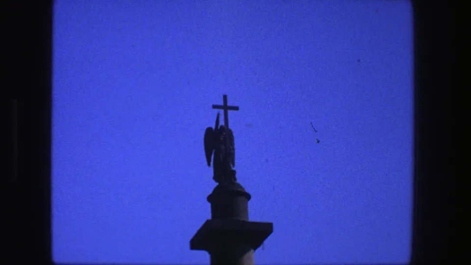 1975 Denmark 8mm frame holding on the silhouetted religious figure and cross, with blue sky and minor film dust visible.