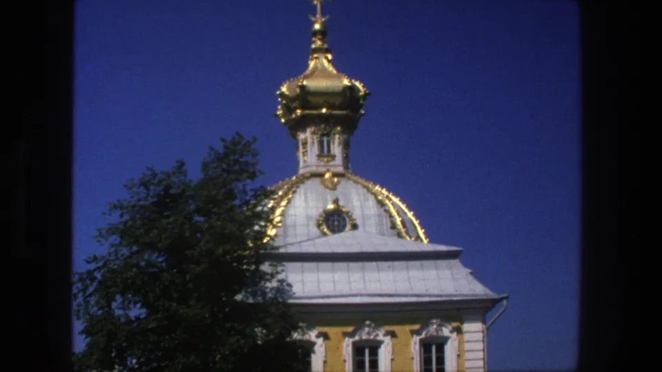 1975 Denmark 8mm frame showing an ornate golden church dome, cross finial, pale roof, yellow facade, and tree foliage.