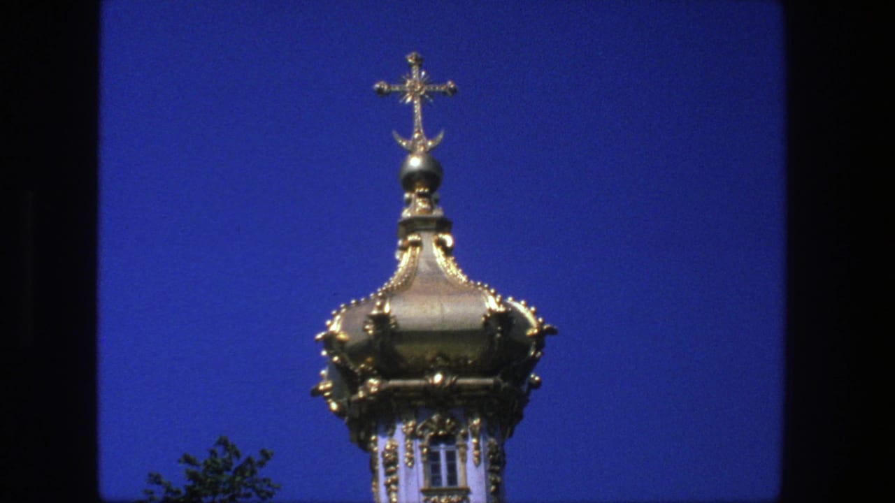 Gilded church dome and cross against a deep blue sky with dark film borders.