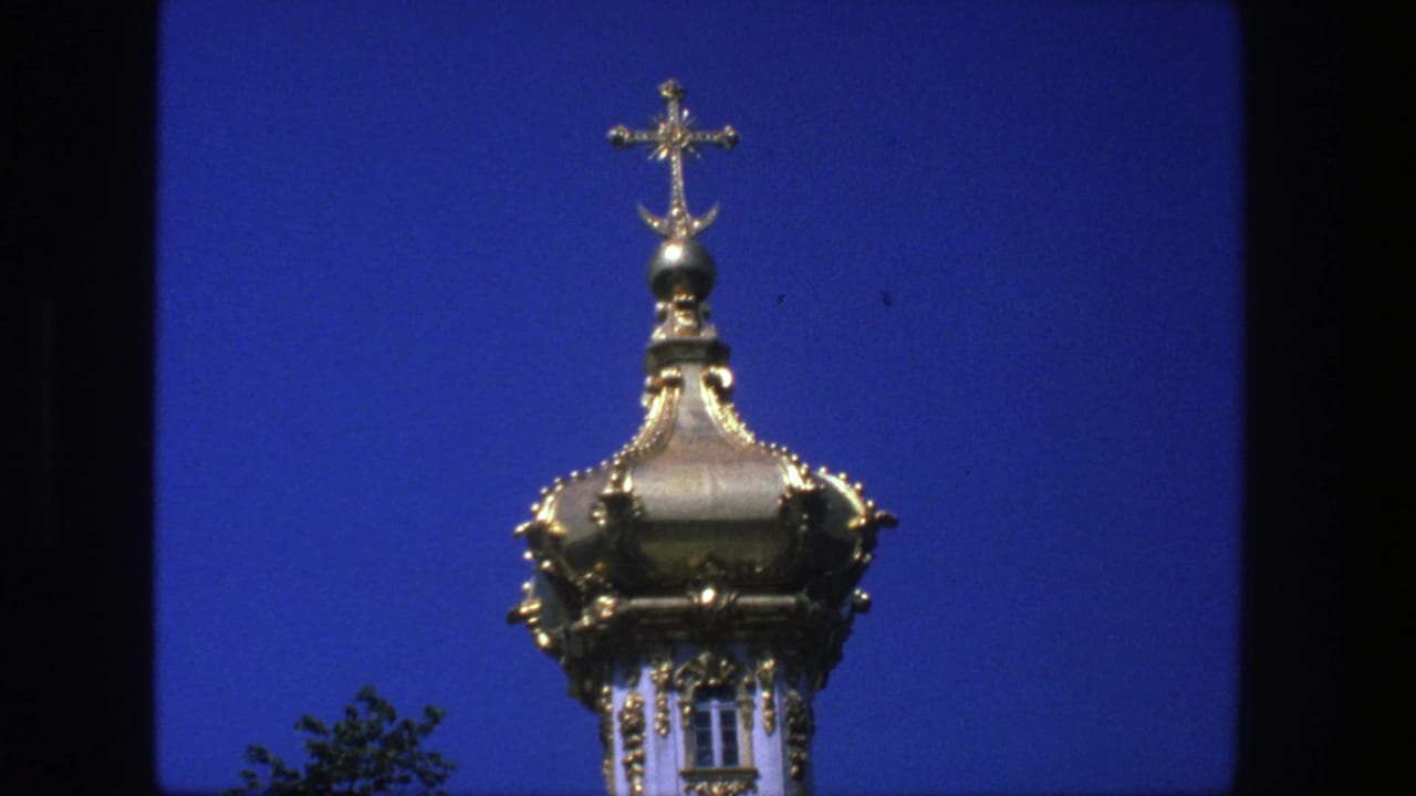 Close 8mm view of a gilded church dome and cross in Denmark, with strong blue sky and slight film softness.