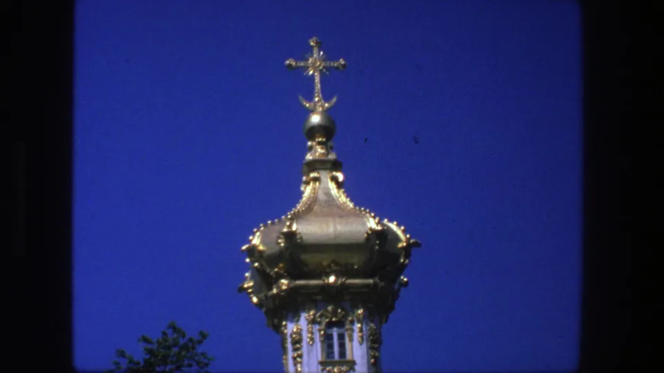 Close 8mm view of a gilded church dome and cross in Denmark, with strong blue sky and slight film softness.