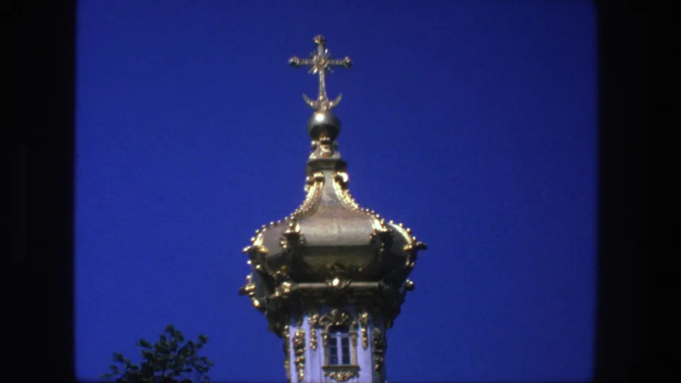 1975 Denmark home-movie still of a gold church dome topped with a cross, with tree leaves visible at the lower edge.