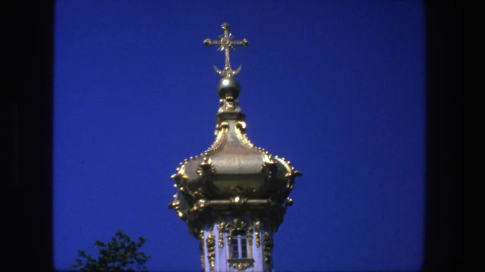 Final 8mm frame holds on the gilded religious dome and cross, with dark film edges and saturated sky color.