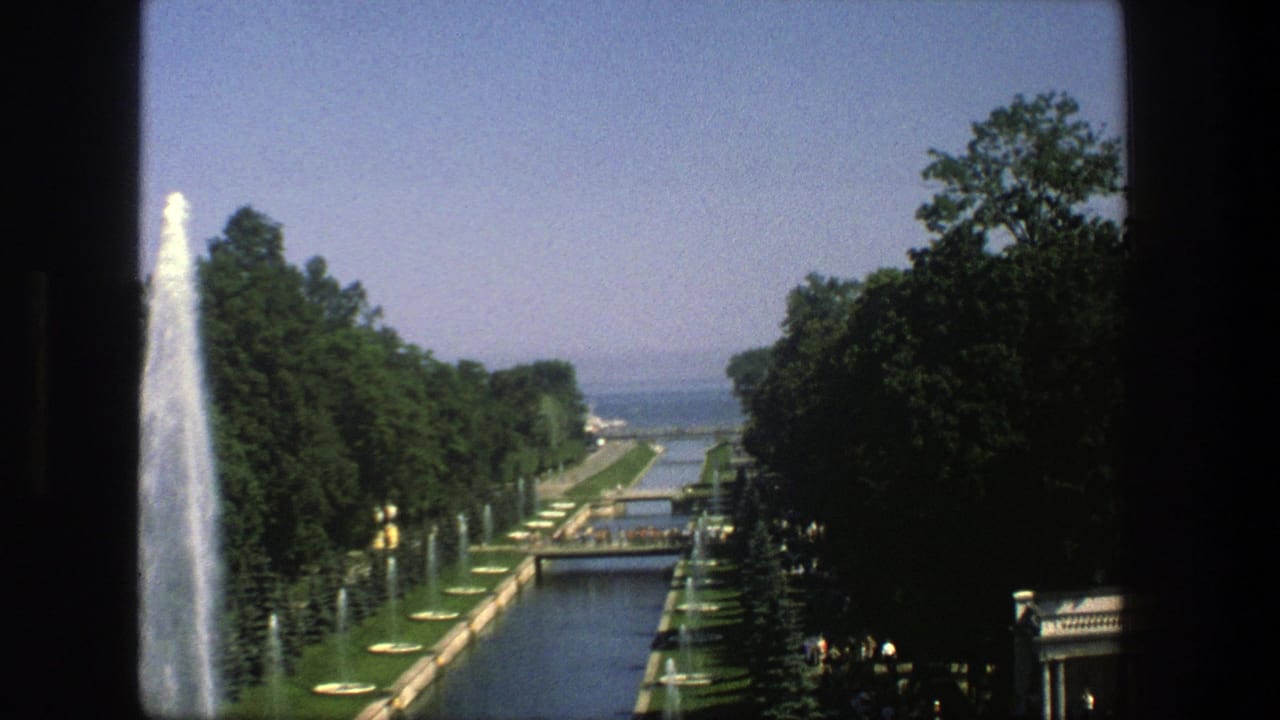 1975 Denmark 8mm view of a formal water channel with tall fountain spray, tree-lined paths, lawns, and distant water.