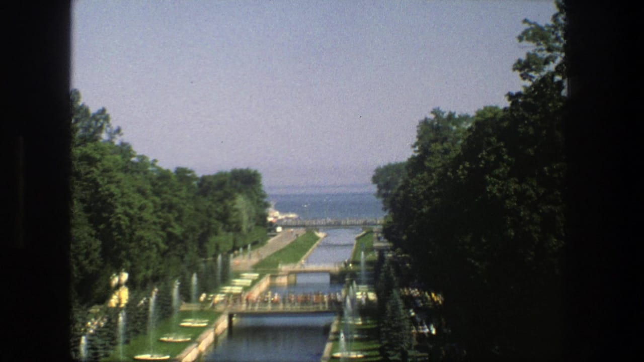 1975 Denmark travel footage frames a formal channel, bridge, fountain jets, trees, lawns, and distant water from a shaded overlook.