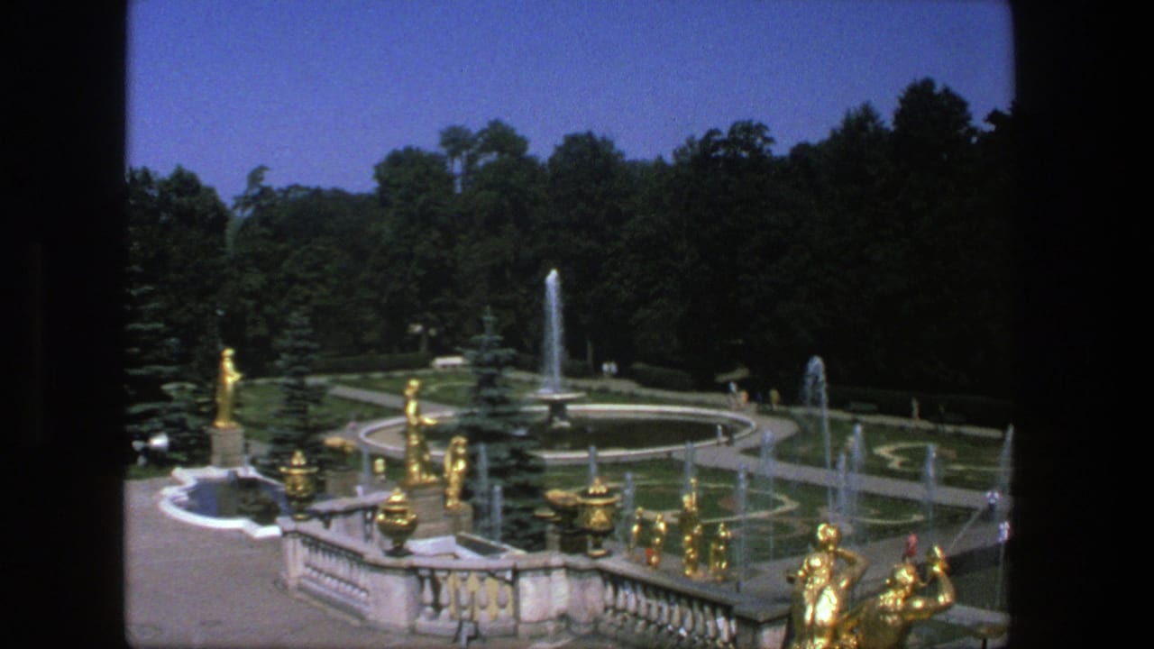 Elevated view of formal gardens with gilded statues, fountains, paths, lawns, and trees.