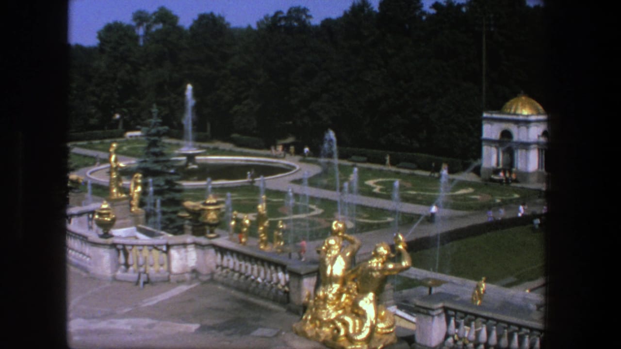1975 8mm view in Denmark of a formal garden with gold sculptures, spraying fountains, clipped lawns, trees, and distant visitors.