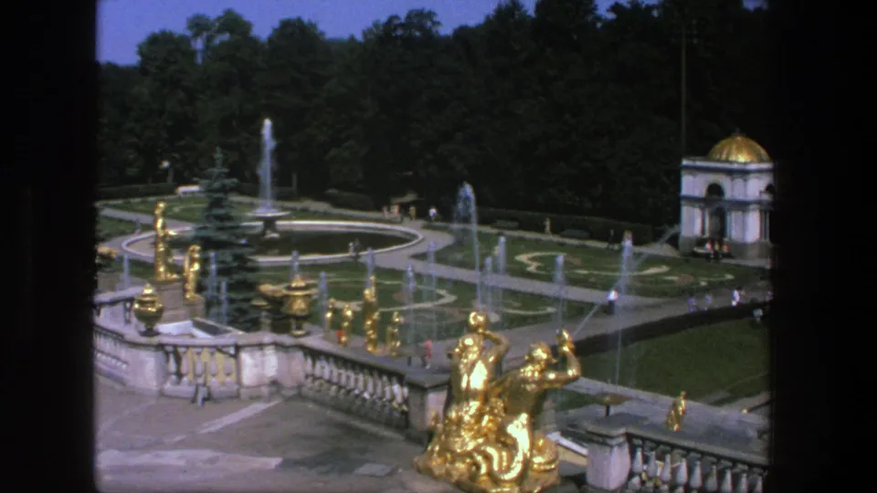 1975 8mm view in Denmark of a formal garden with gold sculptures, spraying fountains, clipped lawns, trees, and distant visitors.