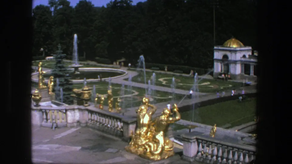 Elevated 1975 Denmark garden shot with gilded terrace figures, fountain jets, geometric lawns, a domed pavilion, and small visitors.