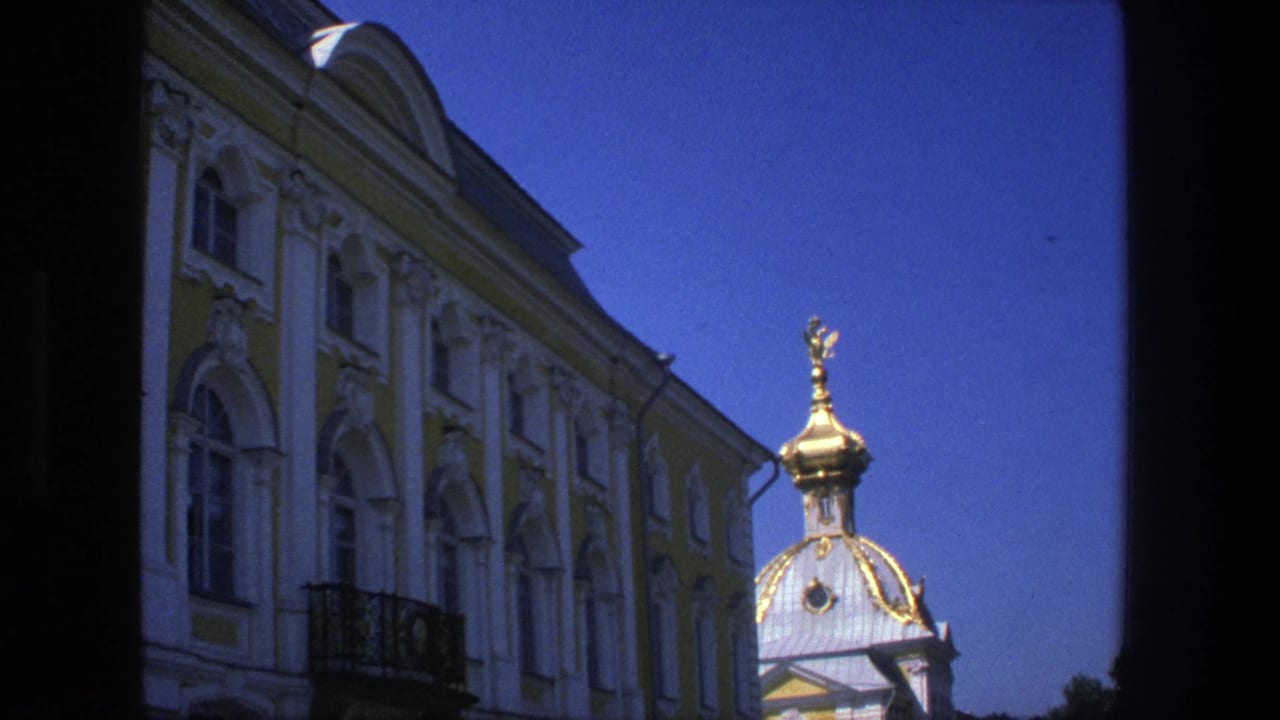 1975 Denmark 8mm frame with a pale yellow ornate facade, white moldings, arched windows, and a gilded dome at right.