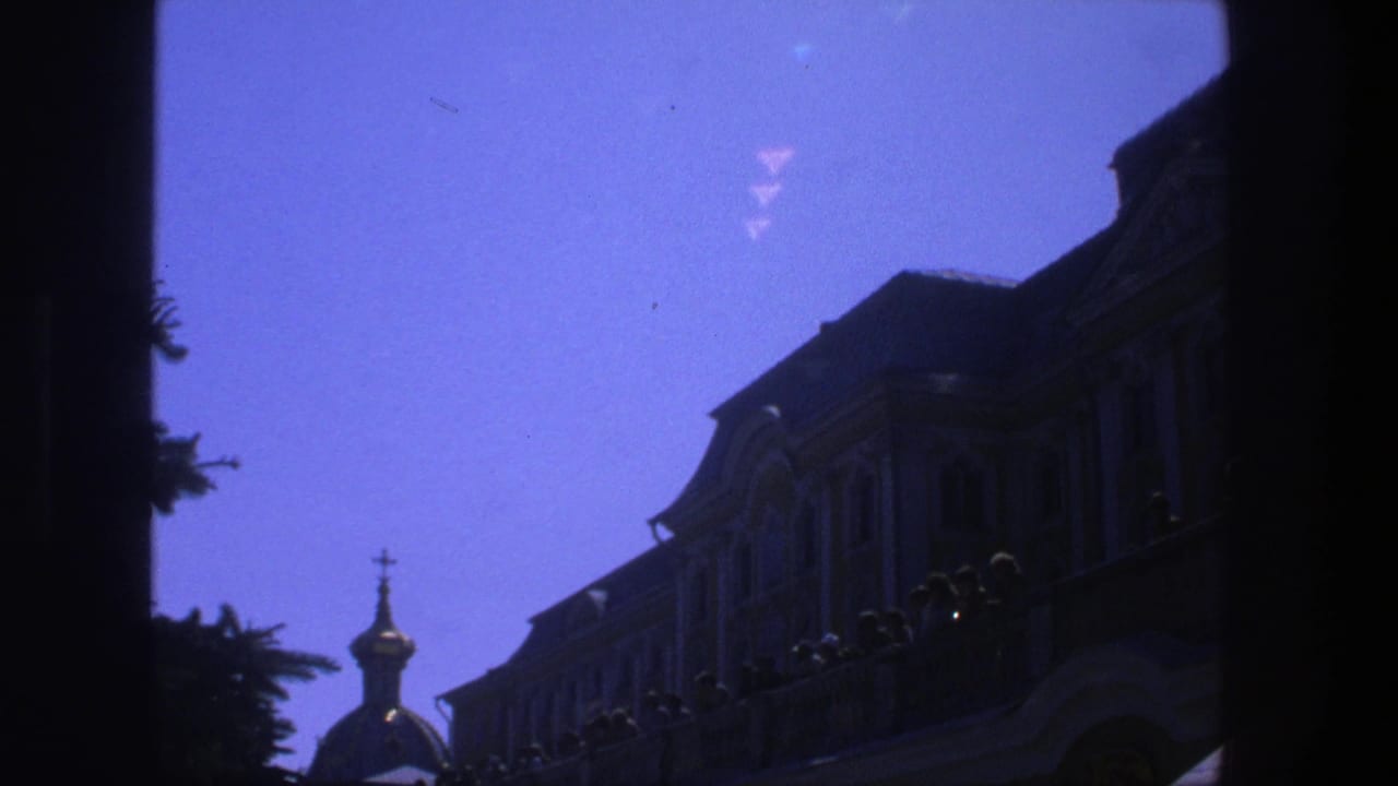 Dark doorway framing a European facade, balcony silhouettes, and a small domed cupola under violet-blue sky.