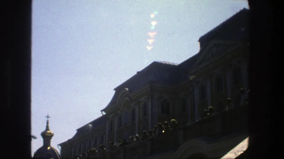1975 Denmark 8mm frame showing a brighter pale sky, a small gilded cupola, grand facade details, and balcony viewers in silhouette.