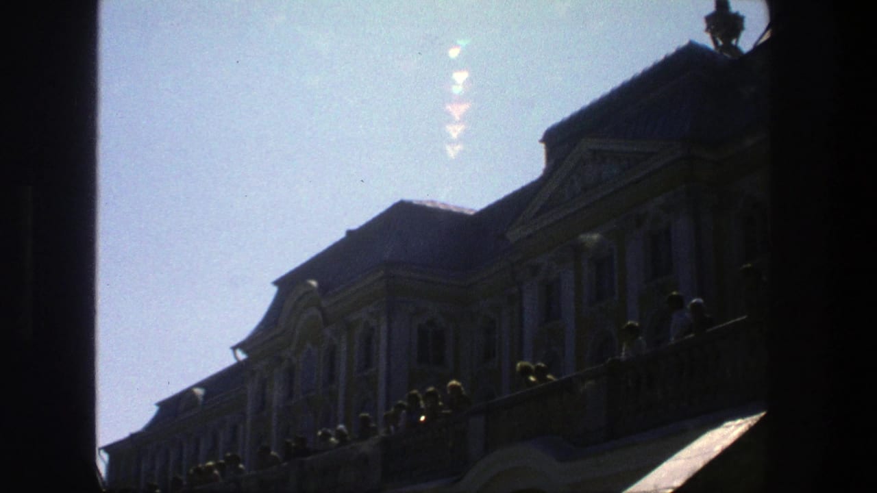 Silhouetted palace facade with visitors along a balustrade under a bright sky.