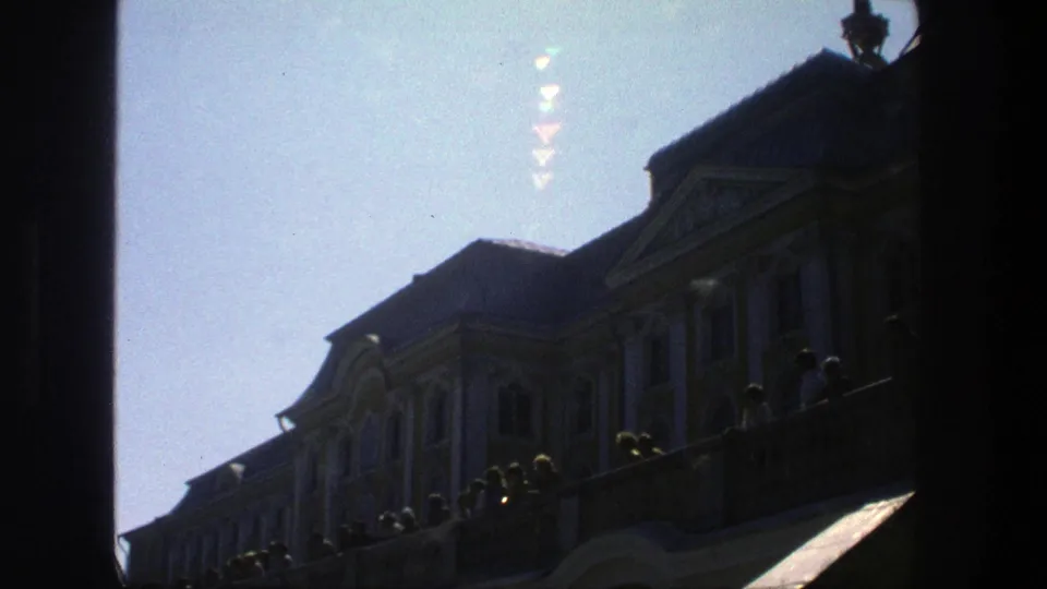 1975 Denmark 8mm frame showing a palace facade in silhouette, with visitors gathered along a terrace below a bright sky.