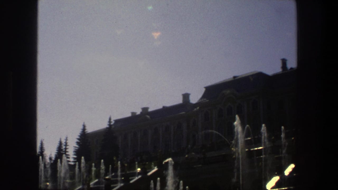 Ornate building partly silhouetted behind fountain jets and dark film-frame borders.