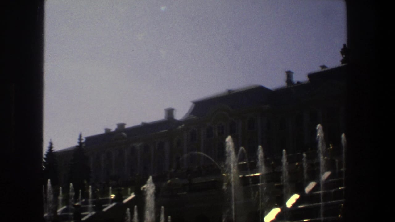 Large formal building behind multiple fountain streams with trees at the edges.