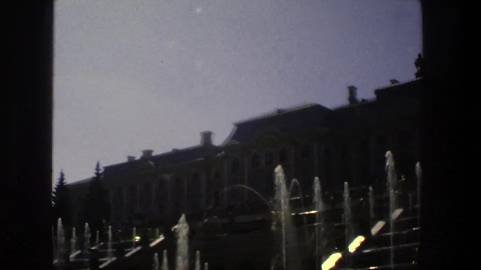 1975 Denmark 8mm frame of a grand exterior with arched windows, roof chimneys, evergreens, and fountain water spraying in front.