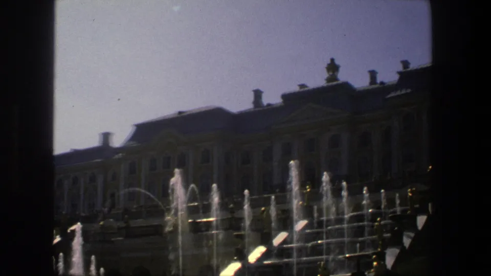 1975 Denmark 8mm frame showing a closer palace-like facade, dark roofline, arched windows, and bright fountain jets in the foreground.