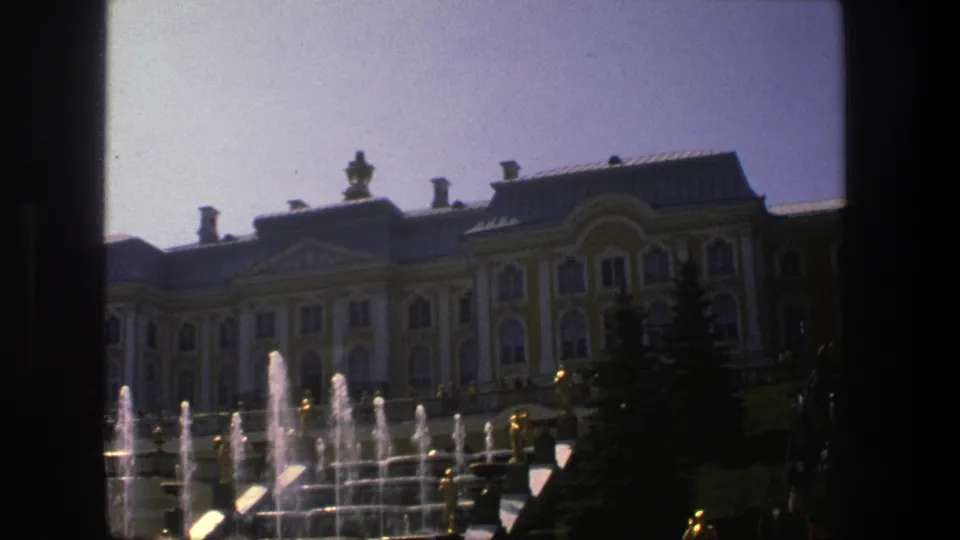 1975 8mm view in Denmark of a yellow-and-white palace facade behind spraying fountains and formal grounds.