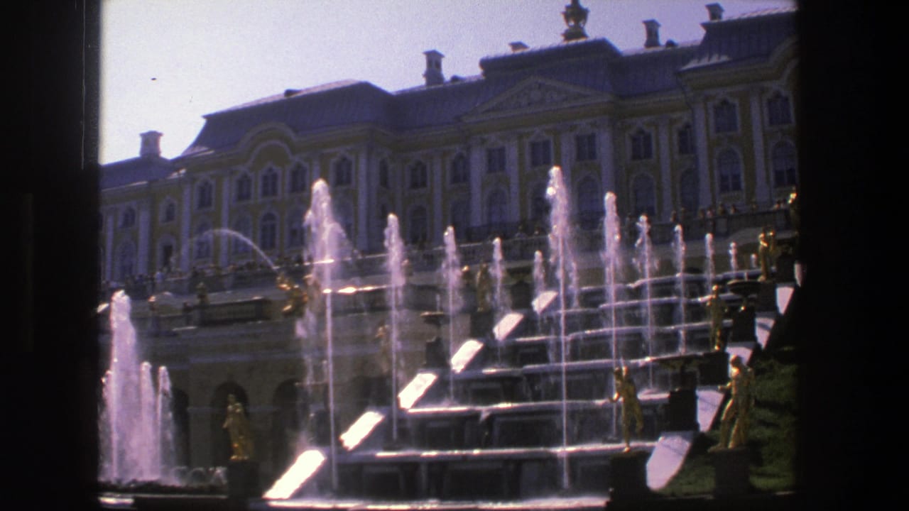 1975 8mm Denmark frame of a formal fountain terrace, gilded figures, and an ornate palace facade seen from a visitor viewpoint.