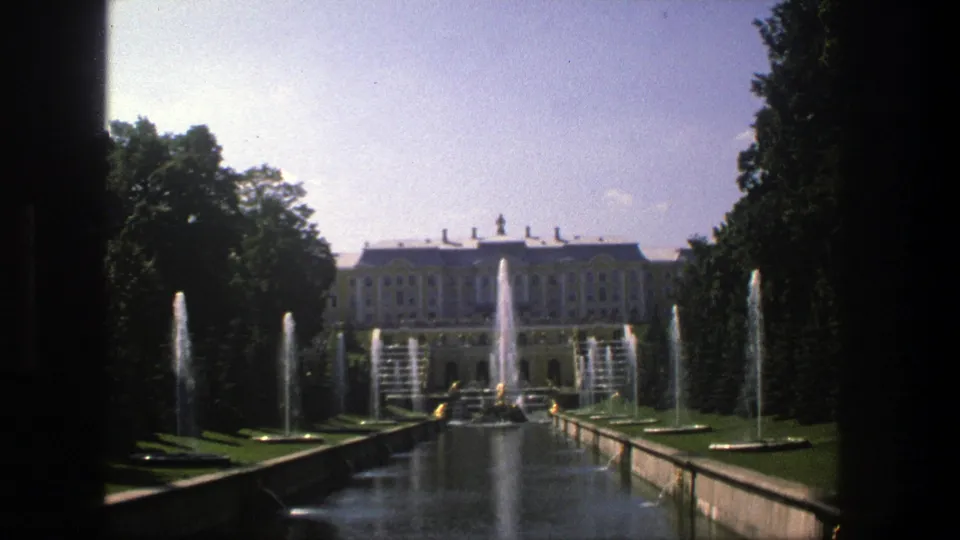 1975 Denmark 8mm frame looking along a formal reflecting pool with fountain jets, trees, lawns, and a distant palace-like building.