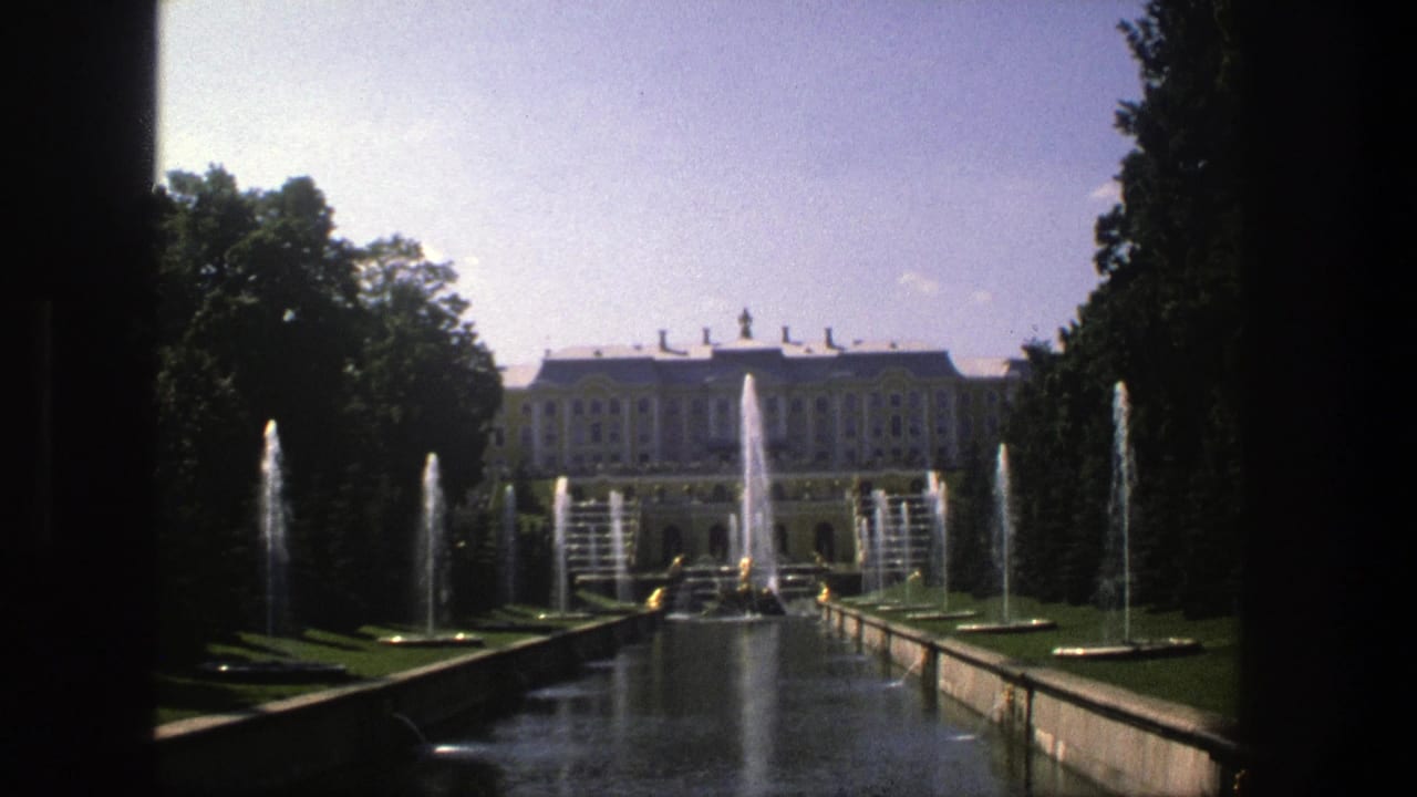 1975 Denmark 8mm frame showing a formal garden canal, fountain jets, trees, and a distant palace-like building.