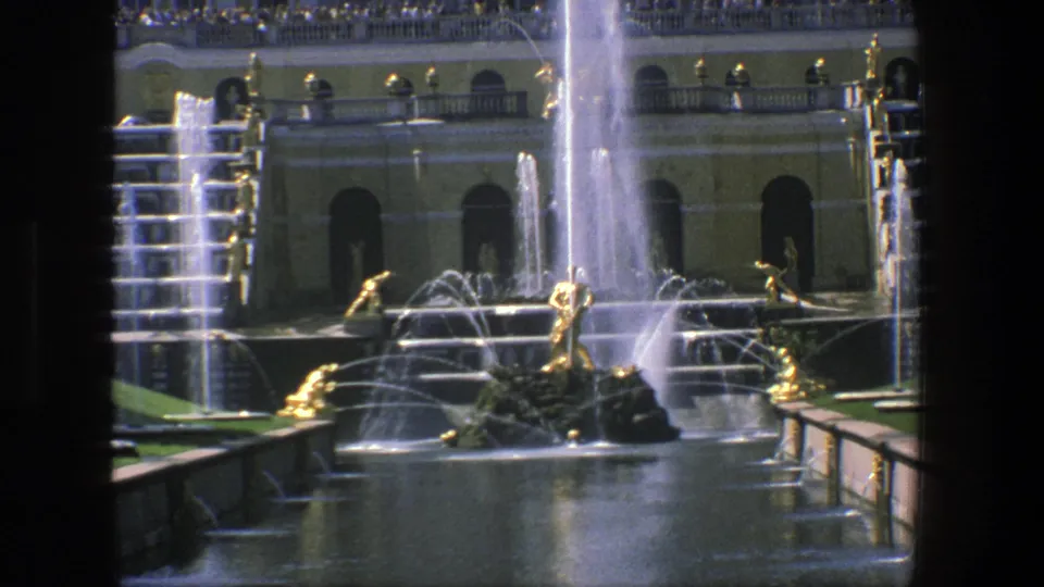 Closer 1975 Denmark frame of gilded fountain figures, cascading water, terrace arches, balustrade, and distant visitors.