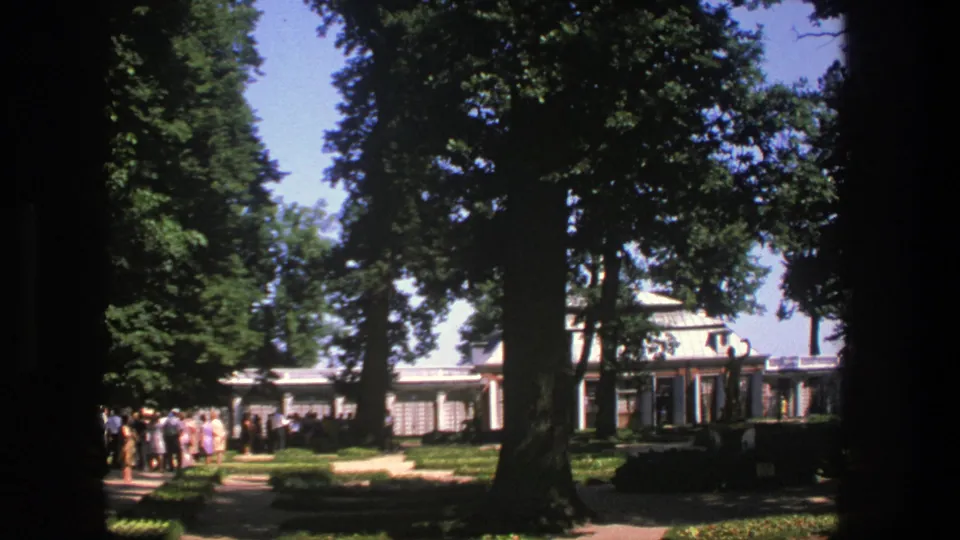 1975 Denmark 8mm frame showing the line shifted toward the left edge, with tall trees and manicured grounds in view.