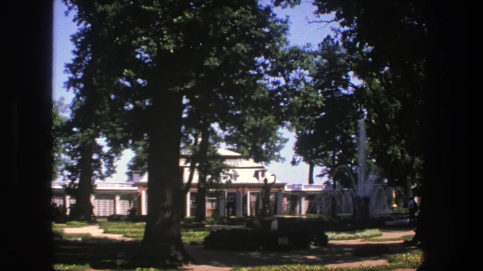 1975 Denmark home-movie view of a shaded park, formal garden path, classical-style building, and fountain spray.