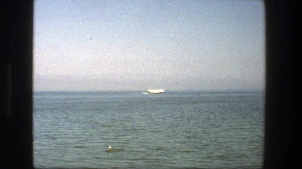 1975 Denmark seaside frame with a small white boat near the horizon and gentle ripples across the water.