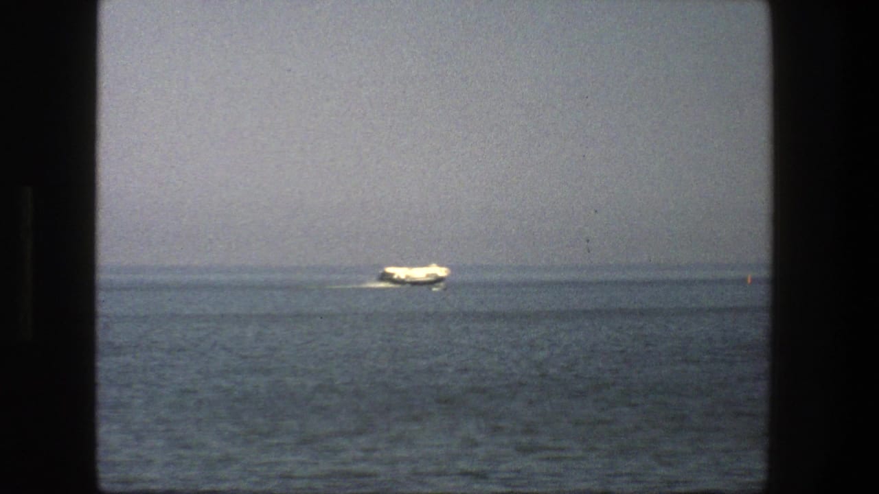 White boat crossing calm water beneath a hazy horizon.