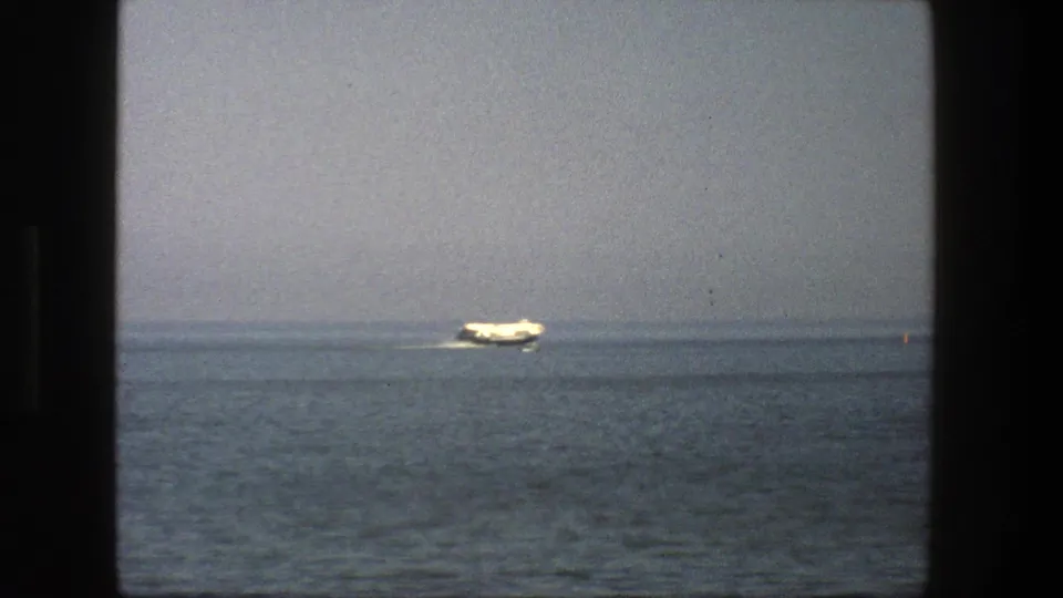 1975 Denmark 8mm frame showing a white boat on blue-gray water, seen through dark frame edges under a hazy sky.
