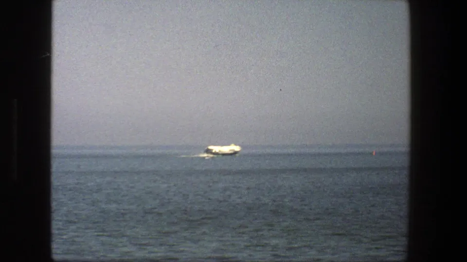 1975 Denmark 8mm frame with a white boat traveling rightward across a foggy blue-gray expanse of water.