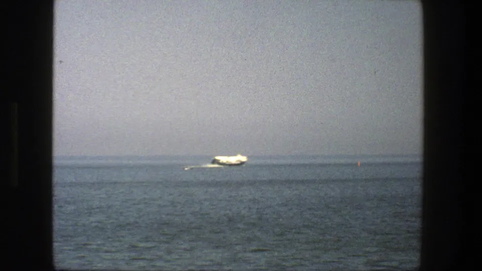 1975 Denmark 8mm frame showing a distant white boat near the horizon and a small red buoy on calm water.