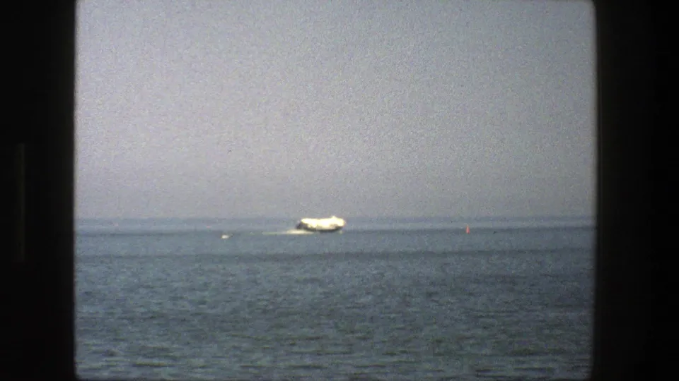 1975 Denmark 8mm frame of a white boat crossing calm water, with a red buoy visible near the right side.