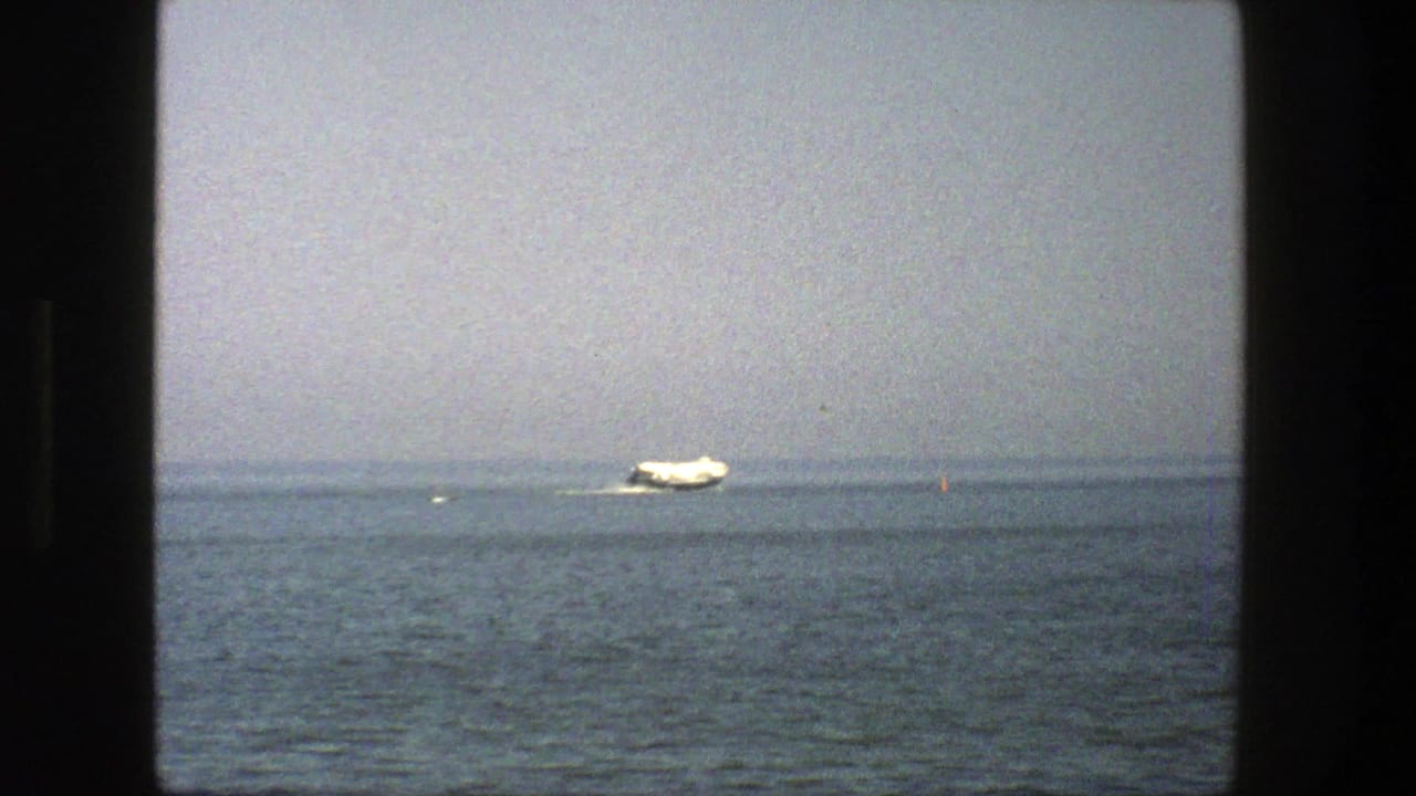 White boat crossing calm water beneath a hazy sky with dark film borders.