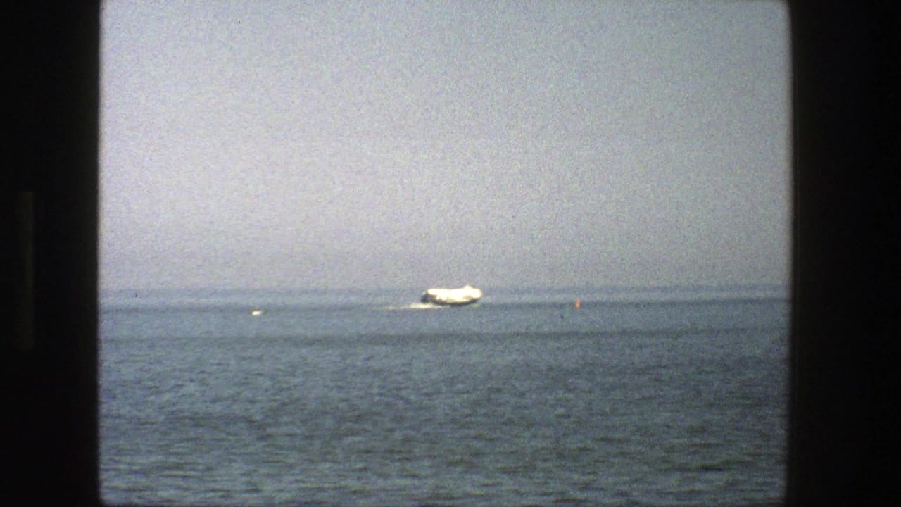 Small white boat on open water with a faint shoreline and hazy sky.