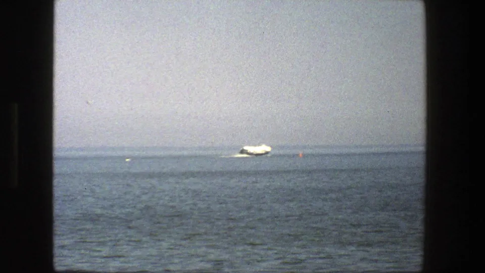 The white boat appears farther across calm Danish water, with visible 8mm grain, soft focus, and a faint horizon line.