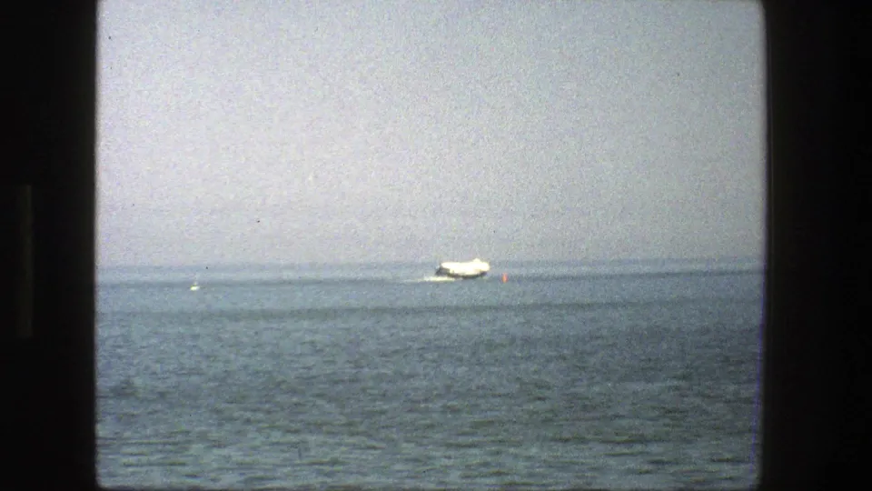 A distant white boat passes near a small red buoy on calm water in this 1975 Denmark 8mm home-movie frame.