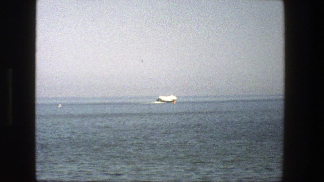 Small white boat on calm sea seen through a dark window frame.