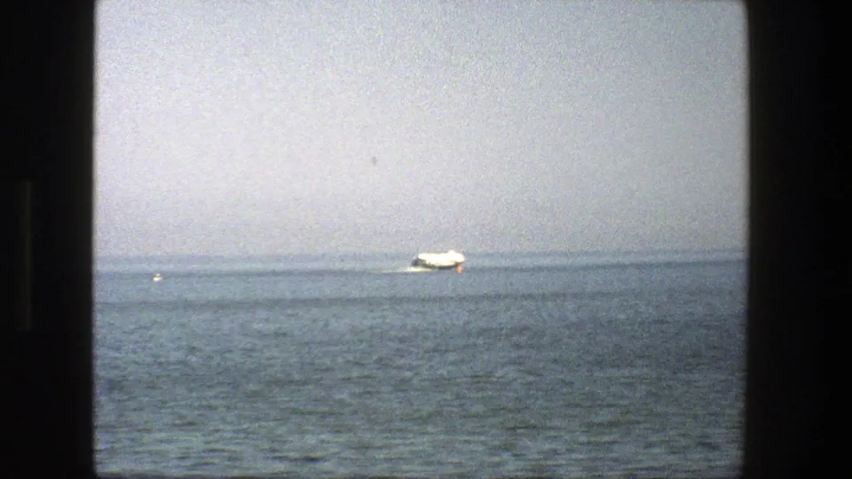 1975 Denmark 8mm frame showing a small white boat on calm open water beneath a hazy sky, divided by a dark window frame.
