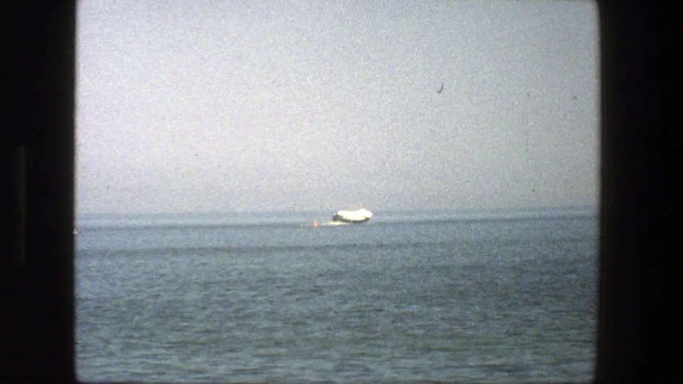 1975 Denmark 8mm frame showing a small white boat crossing blue-gray water with a pale hazy sky above.