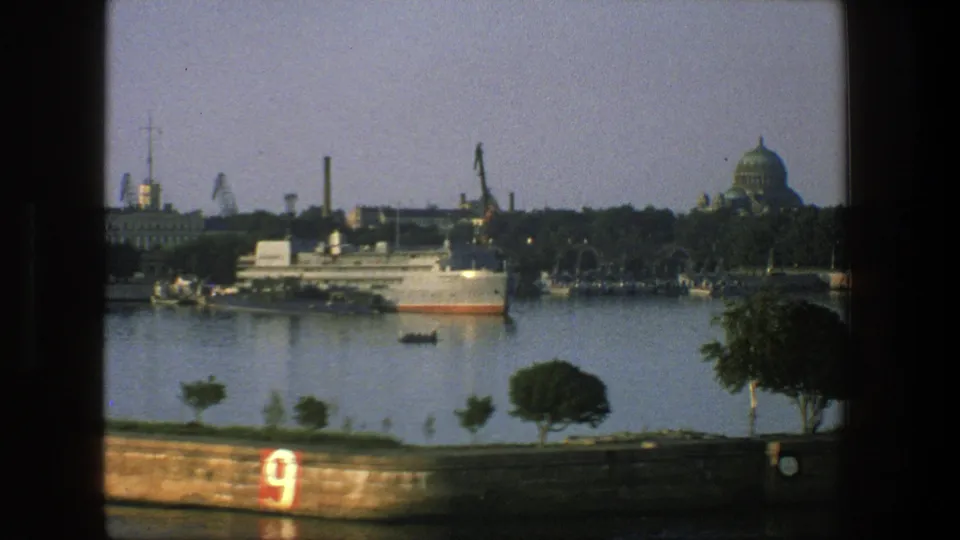 1975 Denmark 8mm frame with a red number 9 on the foreground seawall, calm harbor water, docked vessel, cranes, and distant dome.