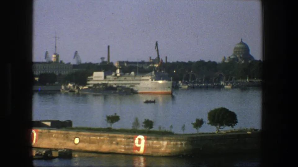 1975 Denmark harbor frame showing the docked vessel across the channel, the red 9 seawall marker, cranes, trees, and a distant domed structure.