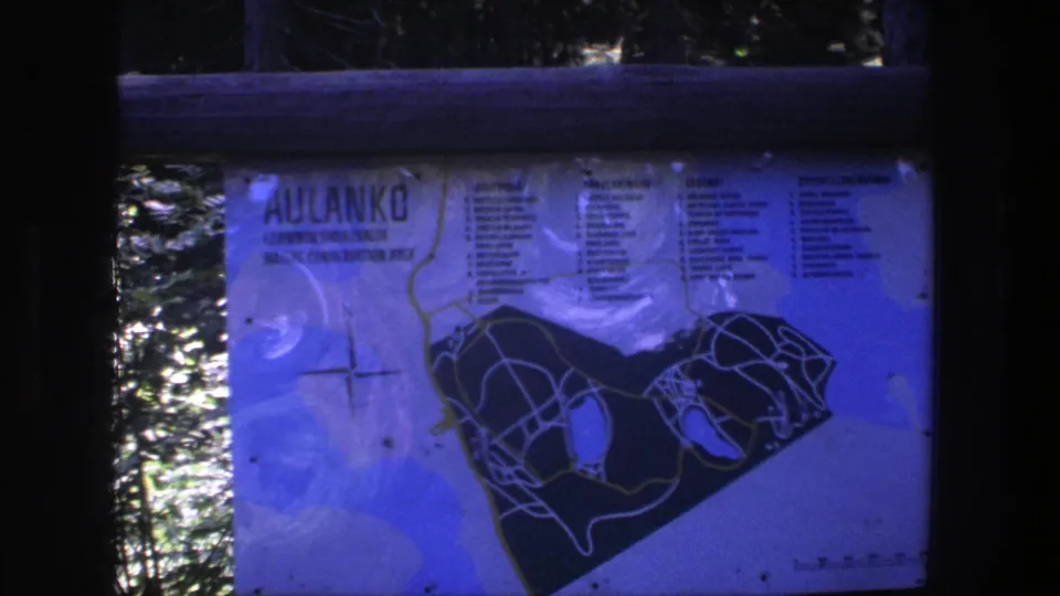 Close view of an Aulanko conservation-area map with a compass graphic and trail markings, filmed in blue-shifted 8mm color.