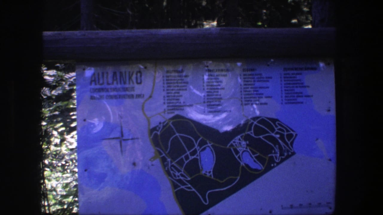 Aulanko park map sign behind wooden rails with trees and bright foliage in the background.